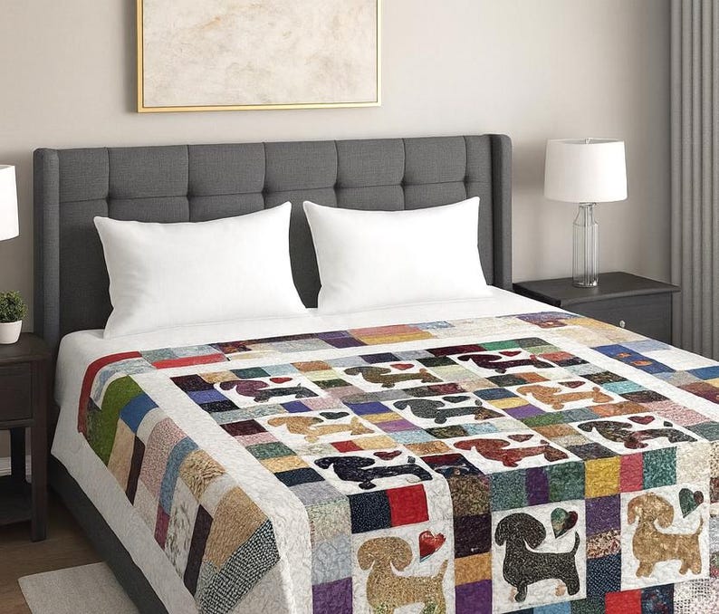Pu&ograve; includere: Una colorata trapunta patchwork con un motivo ripetuto di cani bassotti. La trapunta &egrave; realizzata con vari quadrati di tessuto nei toni del rosso, blu, verde e marrone. La trapunta &egrave; su un letto con cuscini bianchi e una testiera grigia.