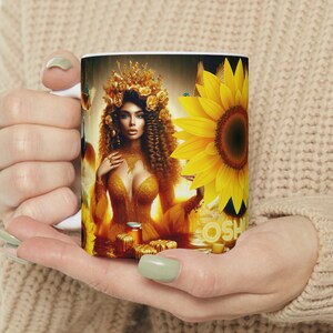 May include: White ceramic mug with a colorful image of a woman with a crown of flowers and a sunflower. The woman is wearing a yellow dress and is surrounded by sunflowers.