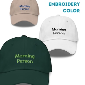 May include: Three baseball caps with the text "Morning Person" embroidered on the front. The caps are in beige, white, and dark green. The text is in blue, black, and light green.
