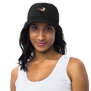 Op de afbeelding: Zwarte denim baseballcap met een klein geborduurd vogelontwerp in bruin- en beigetinten. De pet wordt gedragen door een persoon die een witte tanktop draagt.