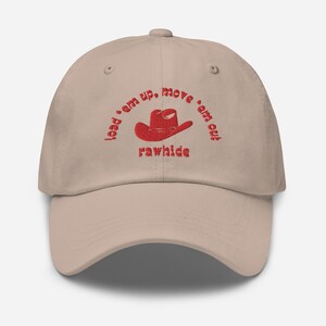 May include: A beige baseball cap with red embroidered text that reads "load 'em up, move 'em out, rawhide" and a red cowboy hat graphic.