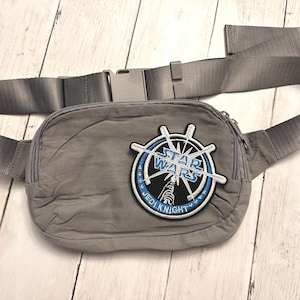 May include: Gray fanny pack with an adjustable strap and buckle closure. The pack features a Star Wars Jedi Knight patch with a blue and white design. The fanny pack is made of a lightweight material.