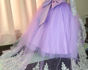 May include: A lavender tulle dress with a silver lace trim and a satin bow. The dress has long sleeves and a button-up back.