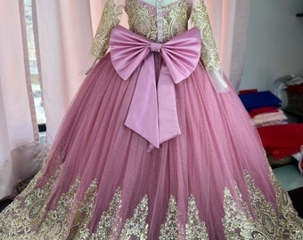May include: A pink tulle dress with gold lace detailing and a large pink satin bow at the back. The dress has a button closure down the back.