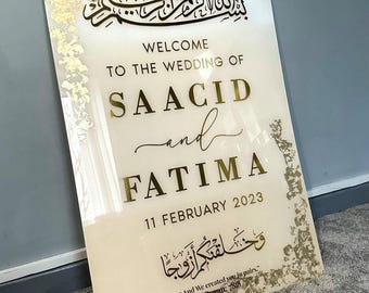 Puede incluir: Un letrero de bienvenida de boda con letras y detalles dorados. El letrero dice "Bienvenida a la boda de Saacid y Fatima, 11 de febrero de 2023". Incluye caligrafía árabe y una cita del Corán.