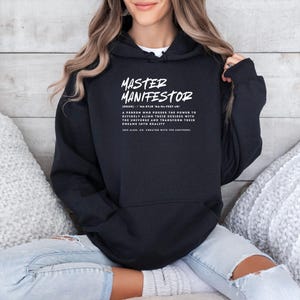 May include: Black hooded sweatshirt with the text "MASTER MANIFESTOR" and a definition of the word. The text is in white.