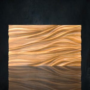 Könnte beinhalten: Rechteckiges Wandkunstwerk aus Holz mit einem wellenartigen Muster, das in die Oberfläche geschnitzt ist. Das Holz hat eine warme, hellbraune Farbe mit dunkleren braunen Reflexen darunter. Der Hintergrund ist eine dunkle, strukturierte Oberfläche.