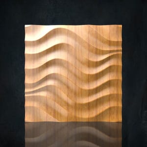 Puede incluir: Panel rectangular de madera clara con un diseño de ondas talladas. La madera muestra vetas visibles y las ondas talladas crean sombras. El panel es probablemente un elemento decorativo de pared, de unos 60 cm x 60 cm.