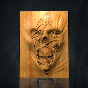 Può includere: Intaglio in legno di un teschio dall'aspetto strappato e angosciato. I lineamenti del teschio sono intagliati in modo intricato, con denti e orbite visibili. Il legno ha un tono caldo e naturale, su sfondo scuro.