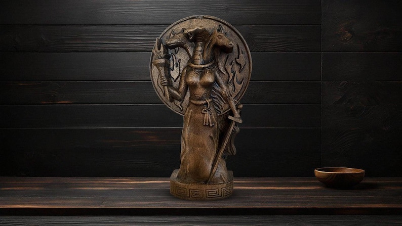 May include: A wooden sculpture of a three-headed goddess holding a torch and a sword. The goddess is standing on a circular base with a decorative pattern.