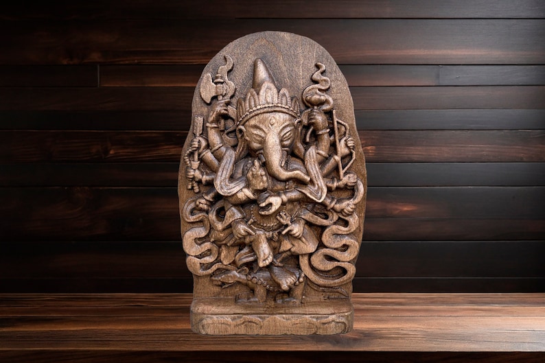 May include: A dark brown wooden carving of the Hindu deity Ganesha. The carving is detailed and intricate, with Ganesha depicted with multiple arms and a trunk. The carving is mounted on a wooden base.