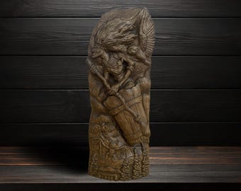 May include: A brown, vertical wooden carving featuring a detailed relief of a figure with flowing hair holding a staff, accompanied by an owl with spread wings. The lower section depicts a bat and forest trees, all rendered in a dark, textured finish.