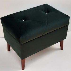 Peut inclure: Un ottoman de rangement en velours vert foncé avec un dessus capitonné et des pieds en bois.