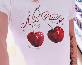 May include: White t-shirt with a cherry graphic. The design includes two red cherries, the text "A lil Fruity vibes", and the phrase "Eat me for breakfast". The shirt has a crew neck.