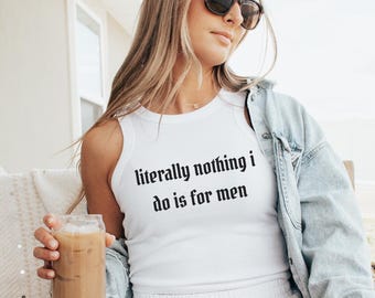 May include: White tank top with the text "literally nothing i do is for men" in black gothic font. The model is wearing sunglasses, white shorts, and a denim jacket. The model is holding a glass of iced coffee.