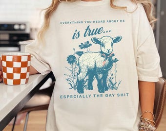 May include: Cream-colored t-shirt with a blue illustration of a lamb surrounded by flowers. The text on the shirt reads "EVERYTHING YOU HEARD ABOUT ME is true... ESPECIALLY THE GAY SHIT."