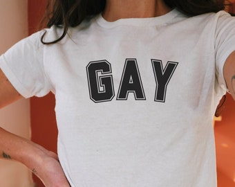 May include: White t-shirt with the word "GAY" printed in black block letters.