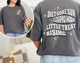 May include: Dark gray t-shirt with the text "Diet Coke Sun Lexapro Moon Little Treat Rising" on the back. A small graphic of a soda can is on the front. The shirt is a relaxed fit.