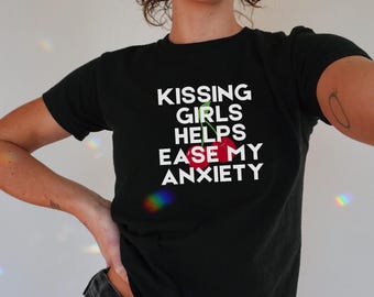 May include: Black t-shirt with the text "KISSING GIRLS HELPS EASE MY ANXIETY" in white, with a red cherry graphic. The shirt is short-sleeved and made of a soft material.