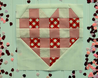 May include: A pink and white gingham heart-shaped quilt block with a white background. The block is made up of squares of pink and white gingham fabric, with the pink squares being larger than the white squares.