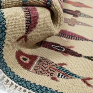 May include: Beige rug with a repeating fish pattern in shades of red, blue, and black. The rug has a teal border and a fringe edge. The fish design is stylized and detailed.