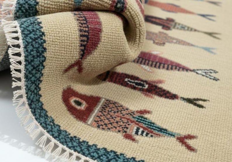 May include: Beige rug with a repeating fish pattern in shades of red, blue, and black. The rug has a teal border and a fringe edge. The fish design is stylized and detailed.