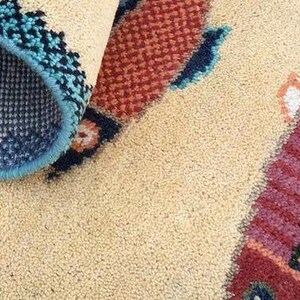May include: Beige rug with a fish design. The fish is primarily red with black and orange stripes. The rug's border is teal and navy blue with a geometric pattern. The underside of the rug is visible, showing a navy blue mesh.