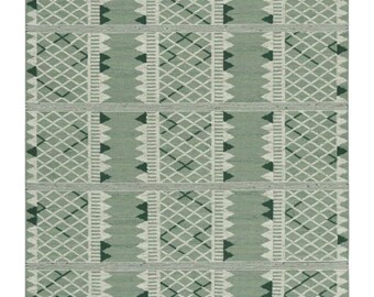 May include: A rectangular, sage green rug with a geometric pattern. The design features rows of diamond shapes, zigzags, and triangles in white and dark green. The rug has a textured appearance, suggesting a woven construction.