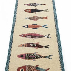 May include: A rectangular beige rug with a repeating pattern of colorful fish. The fish are in various colors, including red, blue, and brown, and have detailed patterns. The rug has a blue border with a geometric design.