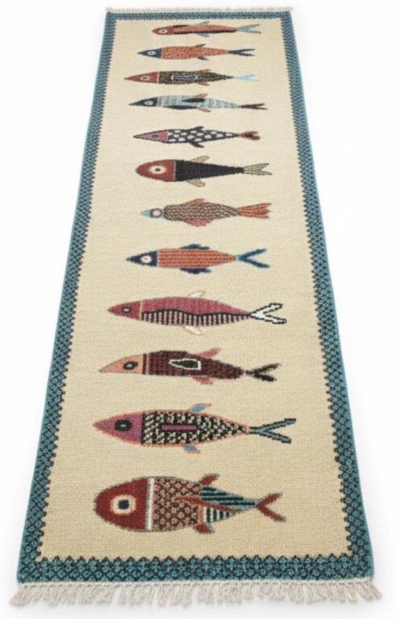 May include: A rectangular beige rug with a repeating pattern of colorful fish. The fish are in various colors, including red, blue, and brown, and have detailed patterns. The rug has a blue border with a geometric design.