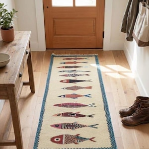 May include: A rectangular beige rug with a repeating pattern of colorful fish. The fish are in shades of red, blue, and brown, with a blue border and fringe. The rug is placed in a hallway.