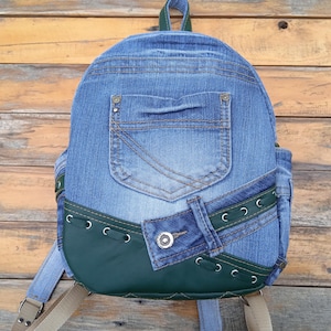 Puede incluir: Una mochila de mezclilla azul con detalles de cuero verde y costuras decorativas. La mochila tiene un bolsillo grande en la parte delantera y un bolsillo más pequeño en la parte superior.