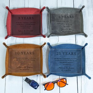 May include: Four leather trays in red, gray, brown, and blue, each with a different anniversary year printed on a central panel. The trays display the years 3, 5, 10, and 25, along with time calculations and names.