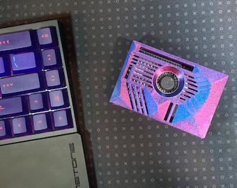 May include: A custom-built computer case with a vibrant pink, blue, and purple geometric design. The case features a central fan and ventilation slots. A backlit keyboard with purple keys is visible on the left.