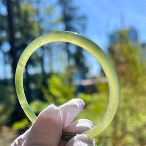 May include: A green jade bangle bracelet. The bracelet is smooth and polished, with a light green color.