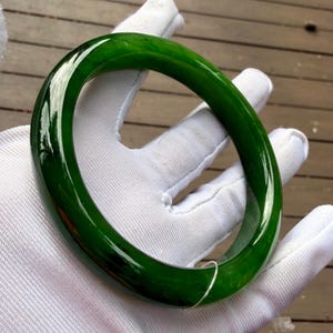 May include: A smooth, polished, circular bangle bracelet in a deep, translucent forest green color. The bangle features a rounded profile with a glossy finish that reflects light across its surface, showcasing a consistent, rich green hue throughout.