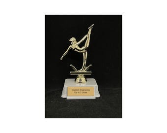 May include: Gold-colored trophy featuring a gymnast in a split pose on a beam. The base is white with the text "Custom Engraving Up to 3 Lines".