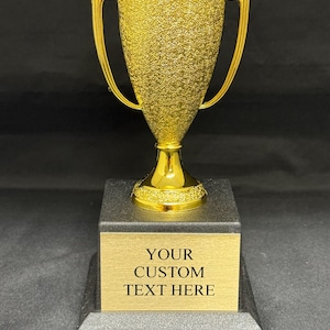 May include: A gold trophy with a textured finish and two handles. The trophy sits on a black base with a gold plaque that reads "YOUR CUSTOM TEXT HERE".