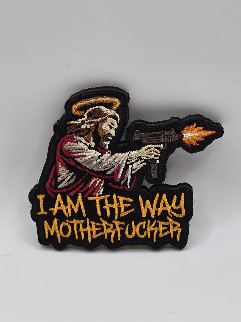 May include: Embroidered patch featuring a depiction of Jesus holding a machine gun with flames. The patch has a black border and the text "I AM THE WAY MOTHERFUCKER" in yellow.