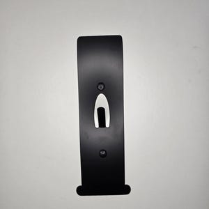 May include: A black metal bracket with a rectangular shape and rounded top. It features a central cutout and two circular holes. The bracket is designed for mounting and has a sleek, minimalist aesthetic.