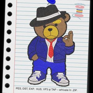 Op de afbeelding: Geborduurd ontwerp van een bruine teddybeer met een zwarte fedora met een witte band, een blauw pak, een rode stropdas en blauwe sneakers. De beer maakt het "oké" handgebaar. Het ontwerp is op gelinieerd papier gespeld.