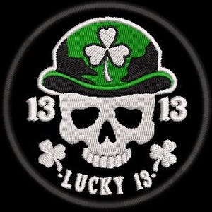 Op de afbeelding: Geborduurde patch met een witte schedel die een groene hoed met een klaver draagt. Het nummer "13" staat aan weerszijden van de schedel, met "LUCKY 13" eronder. De patch is cirkelvormig met een zwarte rand.