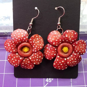 May include: A pair of red and white flower earrings with silver hooks. The flowers have a yellow center and white dots.