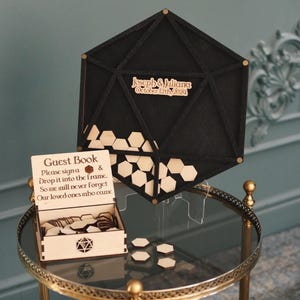 May include: A black hexagonal guest book frame with a wooden box and hexagonal wooden pieces. The frame has the text "Joseph & Juliana October 12th, 2024" engraved on it.
