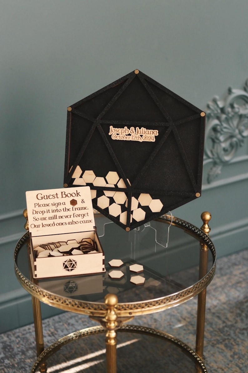 May include: A black hexagonal guest book frame with a wooden box and hexagonal wooden pieces. The frame has the text "Joseph & Juliana October 12th, 2024" engraved on it.