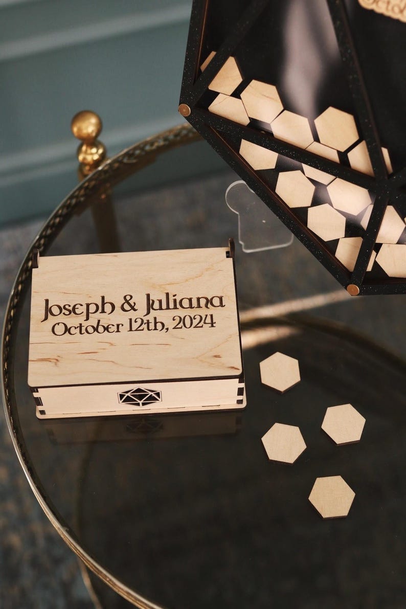 May include: A wooden box with a lid, engraved with the text "Joseph & Juliana October 12th, 2024". The box is sitting on a glass table with several wooden hexagonal pieces scattered around it.