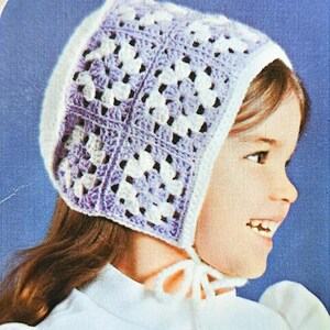 May include: A white crocheted bonnet with a purple and white pattern. The bonnet has a tie at the back.