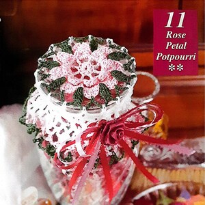 Pode incluir: Um frasco de vidro cheio de potpourri, decorado com um design de pétalas de rosa de crochê e uma fita vermelha. O frasco está etiquetado como "11 Rose Petal Potpourri".