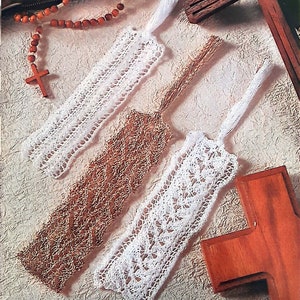 May include: Three white crocheted bookmarks with fringe tassels, one brown crocheted bookmark with a fringe tassel, and a wooden cross with a rosary on a white background.