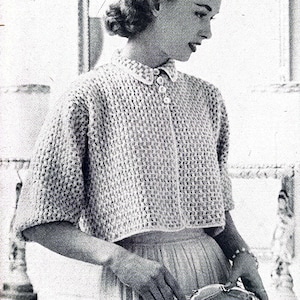 Peut inclure: Gros plan d'une femme portant un pull en crochet blanc avec un col boutonné. Le pull a une texture en nid d'abeille. La femme tient un petit objet orné de couleur argent dans sa main.